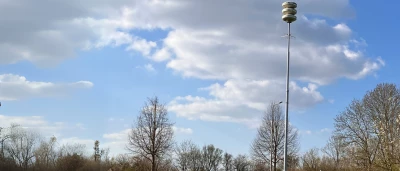 Heldere lucht met enkele wolken boven een sportveld en een paal met sirene.