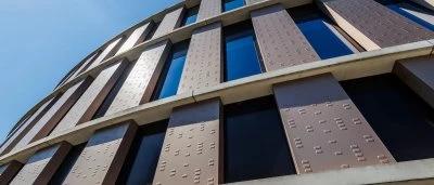 Moderne gevel van een rond gebouw met grote ramen en een heldere blauwe lucht.