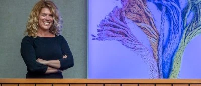 Vrouw met krullend haar glimlacht op een podium voor een kleurrijke achtergrond.