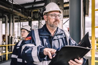 Twee inspecteurs op een industriegebied, een man en een vrouw, met helmen en documenten.