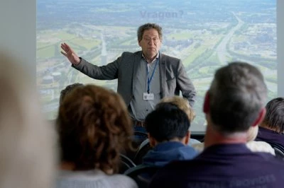 Een man geeft een presentatie voor een publiek, met een projectie op de achtergrond.