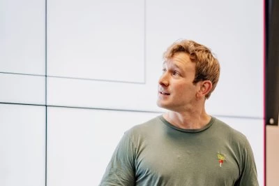 Man in een groen T-shirt geeft een presentatie voor een groot scherm.
