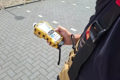 Een persoon houdt een geel meetinstrument vast, staand op een stenen parkeerplaats.