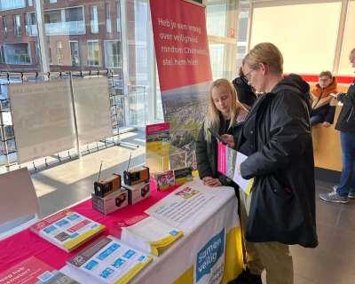 Twee mensen bekijken informatie op een tafel met brochures en promotiemateriaal.