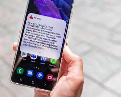Een hand houdt een smartphone met een melding op een straat met stenen.