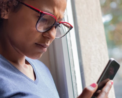 Vrouw met een frons kijkt gefocust naar haar smartphone bij een raam.