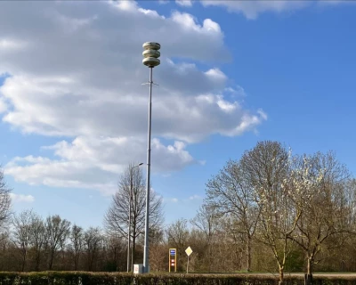 Landschap met een paal sirene onder een blauwe lucht met wolken en bomen.