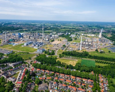 Luchtfoto van een industriegebied met woningen en groene velden op de achtergrond.