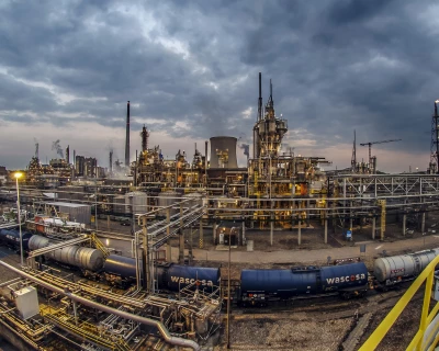 Groot industrieel complex met pijpen en opslagtanks onder een bewolkte lucht.