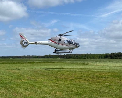 Een witte helicopter zweeft boven een groene veld onder een blauwe lucht.