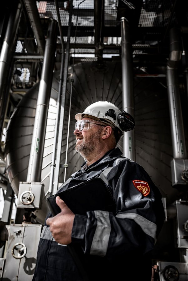 Man in een helm en veiligheidsbril, staande bij industriële apparatuur.